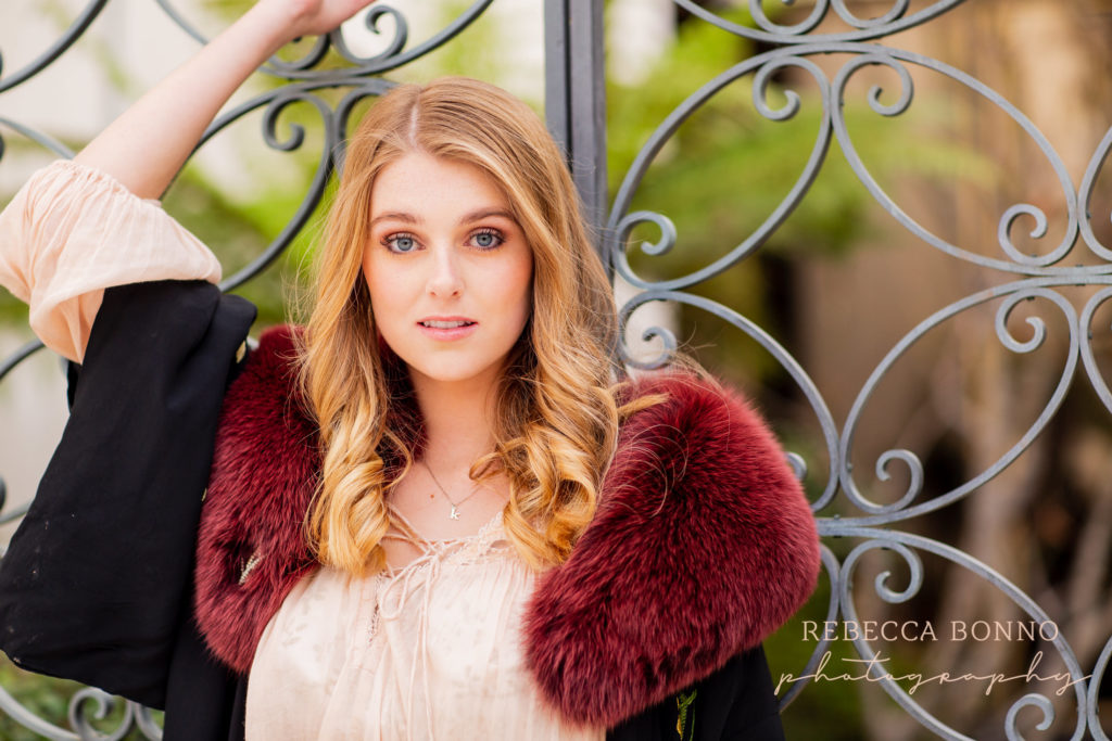 fun senior session with red fur jacket  and rebecca bonno Photography on a iron gate 